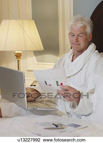 Man sitting in bed using laptop View Large Photo Image Stock Image - Man sitting in bed using laptop. Fotosearch