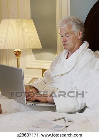 Man sitting in bed using laptop View Large Photo Image Stock Image - Man sitting in bed using laptop. Fotosearch