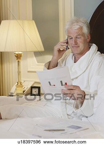Stock Photograph - Man sitting in bed using mobile phone. Fotosearch