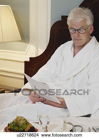 Picture - Man sitting on bed reading document. Fotosearch