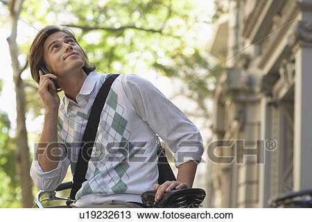 Man sitting on bicycle talking on mobile phone and looking up View Large Photo Image Stock Image - Man sitting on bicycle talking on mobile phone and looking up. Fotosearch