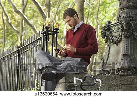 Man sitting on wall using palmtop View Large Photo Image Picture - Man sitting on wall using palmtop. Fotosearch
