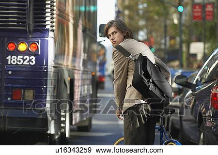 Man standing by bicycle on busy street View Large Photo Image Stock Photo - Man standing by bicycle on busy street. Fotosearch
