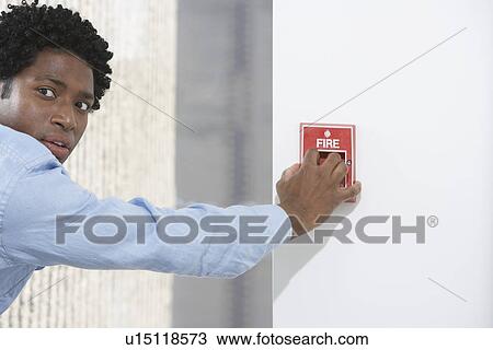 Stock Image - Man starting fire alarm indoors. Fotosearch