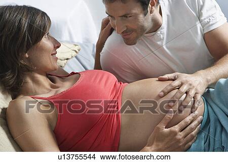 Man touching stomach of pregnant woman lying in bed in bedroom View Large Photo Image Picture - Man touching stomach of pregnant woman lying in bed in bedroom. Fotosearch