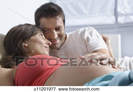 Man touching stomach of pregnant woman lying down in bedroom View Large Photo Image Stock Photo - Man touching stomach of pregnant woman lying down in bedroom. Fotosearch