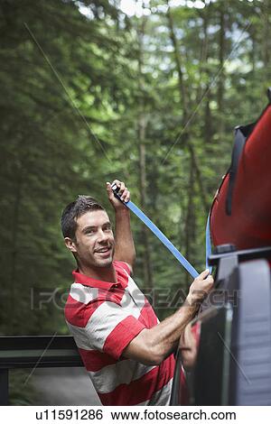 Man tying kayak on car roof in forest View Large Photo Image Stock Photograph - Man tying kayak on car roof in forest. Fotosearch