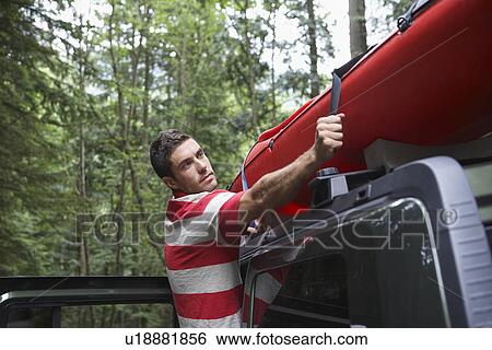 Man tying kayak on car roof in forest View Large Photo Image Stock Photograph - Man tying kayak on car roof in forest. Fotosearch