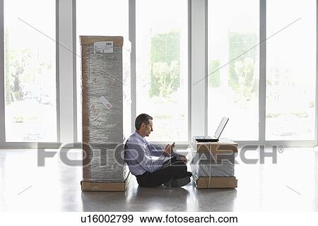 Man using mobile phone and laptop between packages in empty office View Large Photo Image Stock Photo - Man using mobile phone and laptop between packages in empty office. Fotosearch