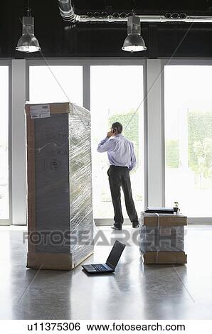 Man using mobile phone by window in office with laptop and packages View Large Photo Image Stock Photograph - Man using mobile phone by window in office with laptop and packages. Fotosearch
