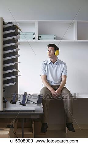 Stock Photo - Man wearing headphones sitting by photocopier. Fotosearch
