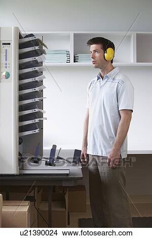 Picture - Man wearing headphones standing by photocopier. Fotosearch