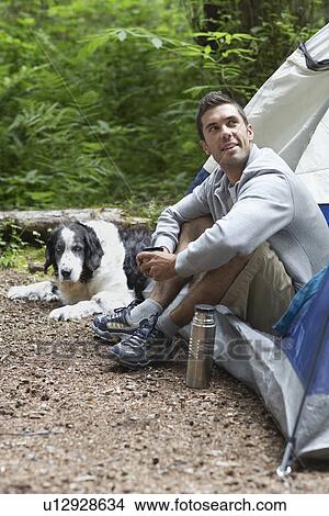 Picture - Man with dog sitting by tent. Fotosearch