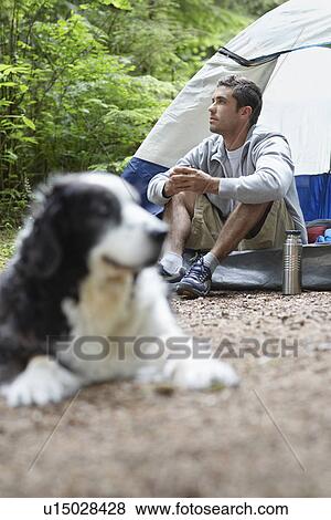 Stock Photo - Man with dog sitting by tent. Fotosearch