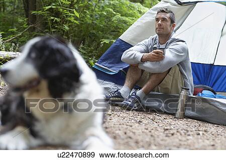 Stock Photo - Man with dog sitting by tent. Fotosearch