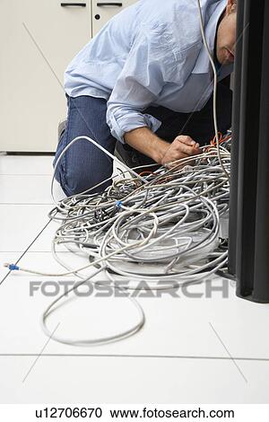 Stock Image - Man working on tangle of computer wires in office. Fotosearch