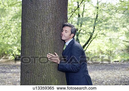 Mid adult business man hugging tree trunk eyes closed View Large Photo Image Stock Photography - Mid adult business man hugging tree trunk eyes closed. Fotosearch