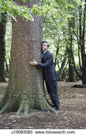 Mid adult business man hugging tree trunk eyes closed View Large Photo Image Stock Photography - Mid adult business man hugging tree trunk eyes closed. Fotosearch