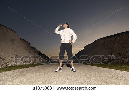 Stock Image - Mid adult man drinking water after jogging. evening. Fotosearch