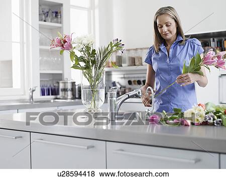 Stock Photo - Mid-adult woman at kitchen sink preparing flowers to be put in vase. Fotosearch