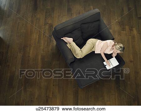 Mid-adult woman lying on sofa leafing through notebook view from above View Large Photo Image Stock Photo - Mid-adult woman lying on sofa leafing through notebook view from above. Fotosearch