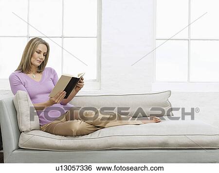 Stock Photograph - Mid adult woman reading book on sofa. Fotosearch