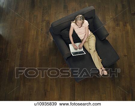 Mid-adult woman sitting on sofa using laptop view from above View Large Photo Image Stock Photo - Mid-adult woman sitting on sofa using laptop view from above. Fotosearch