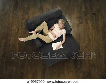 Stock Photo - Mid adult woman sleeping on sofa holding book view from above. Fotosearch