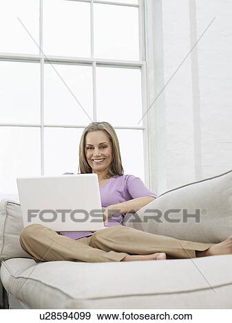 Stock Photo - Mid adult woman using laptop on sofa. Fotosearch