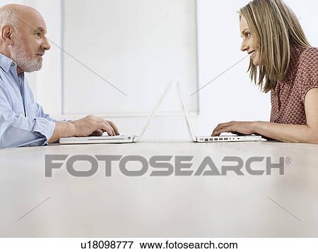 Middle-aged man and mid-adult woman sitting opposite to each other using laptops profile View Large Photo Image Stock Photo - Middle-aged man and mid-adult woman sitting opposite to each other using laptops profile. Fotosearch