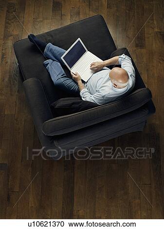 Middle-aged man sitting on sofa using laptop view from above View Large Photo Image Stock Image - Middle-aged man sitting on sofa using laptop view from above. Fotosearch