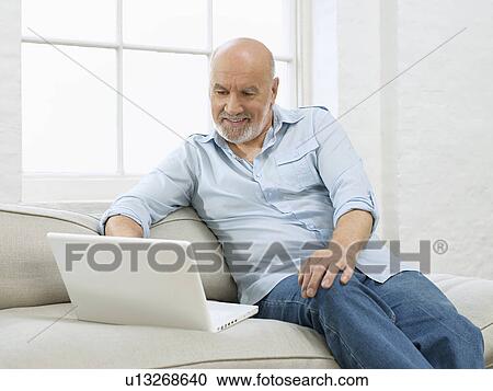Middle-aged man sitting on sofa using laptop View Large Photo Image Stock Image - Middle-aged man sitting on sofa using laptop. Fotosearch