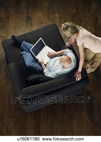 Middle-aged man sitting on sofa using laptop woman leaning and watching view from above View Large Photo Image Stock Image - Middle-aged man sitting on sofa using laptop woman leaning and watching view from above. Fotosearch