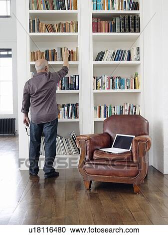 Stock Image - Middle-aged man taking book from shelf back view. Fotosearch