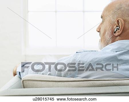 Middle-aged man wearing earphones sitting on sofa and looking to side back view View Large Photo Image Stock Photography - Middle-aged man wearing earphones sitting on sofa and looking to side back view. Fotosearch