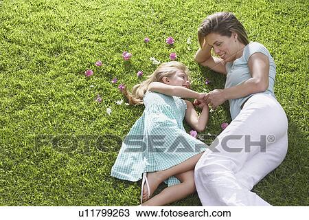 Stock Image - Mother and daughter (5-6) lying on lawn with flowers strewn nearby. Fotosearch