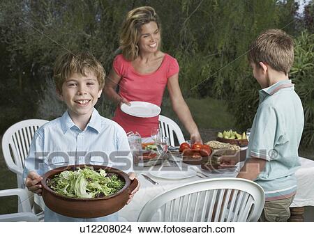 Mother and sons (6-11) preparing dinner table in garden boy holding bowl of salad View Large Photo Image Picture - Mother and sons (6-11) preparing dinner table in garden boy holding bowl of salad. Fotosearch