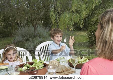Mother and two children (5-6) at table in garden View Large Photo Image Picture - Mother and two children (5-6) at table in garden. Fotosearch