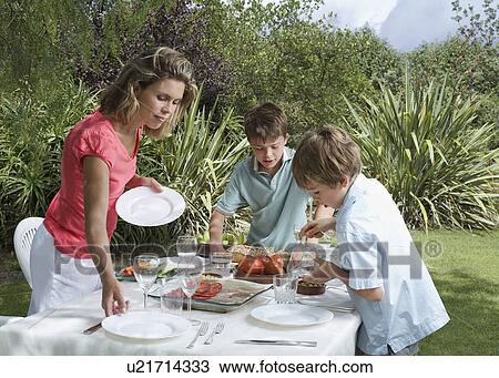 Stock Image - Mother and two sons (6-11) laying dinner table in garden. Fotosearch