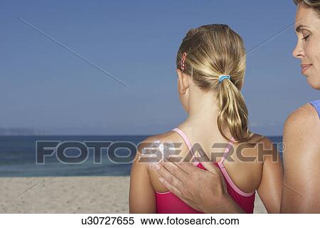 Stock Photography - Mother applying sunscreen to daughter's (5-6) back back view. Fotosearch