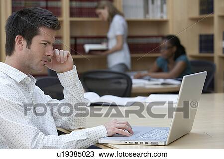 Stock Image - Office worker using laptop in office side view. Fotosearch