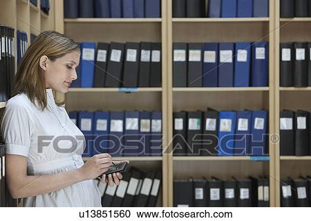 Office worker using palm top standing in file storage room side view View Large Photo Image Stock Image - Office worker using palm top standing in file storage room side view. Fotosearch