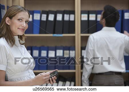Office worker using palm top standing in file storage room colleague standing in background View Large Photo Image Stock Photography - Office worker using palm top standing in file storage room colleague standing in background. Fotosearch