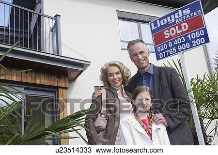 Stock Image - Parents and daughter (7-9) embracing outside new home portrait. Fotosearch