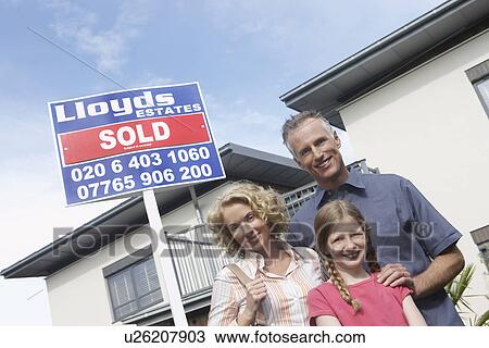 Stock Image - Parents and daughter (7-9) embracing outside new home portrait. Fotosearch