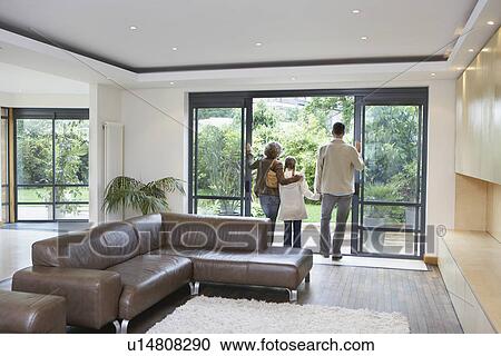 Stock Image - Parents and daughter (7-9) looking through patio door in new home. Fotosearch