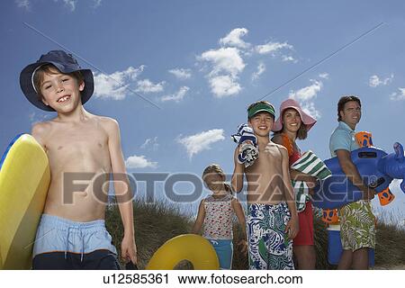 Parents with three children (6-12) carrying beach accessories View Large Photo Image Stock Image - Parents with three children (6-12) carrying beach accessories. Fotosearch
