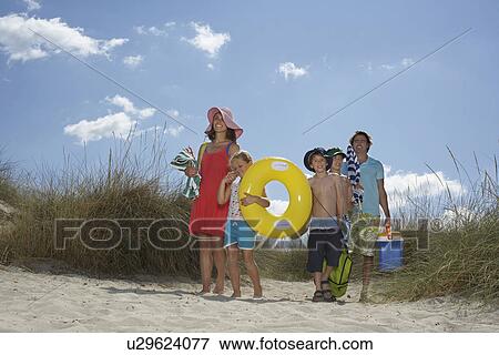 Stock Photo - Parents with three children (6-12) carrying beach accessories. Fotosearch