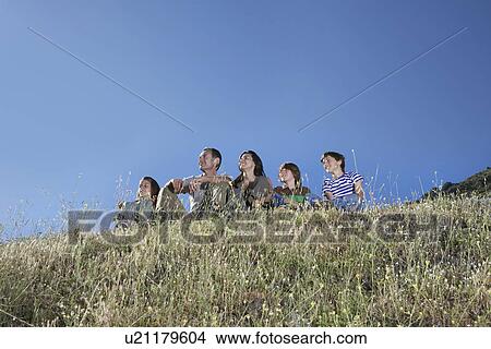 Parents with three children (7-12) sitting on hill looking at view View Large Photo Image Picture - Parents with three children (7-12) sitting on hill looking at view. Fotosearch