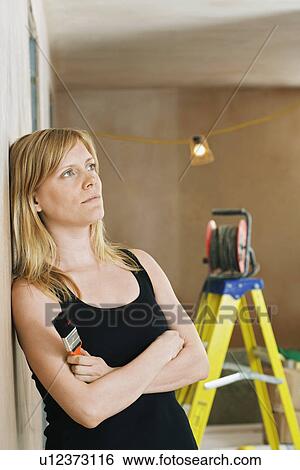 Stock Photograph - Pensive woman leaning against wall ladder in background. Fotosearch